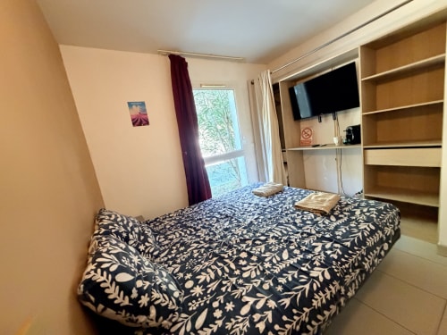 Le Clos d'Aix Studio 11 bedroom with patterned bed, TV, wooden shelving, and garden view windows in Southern France