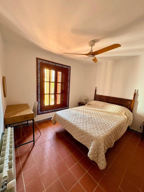 Dormitorio espacioso en Holiday Dreams Ronda con cama de madera, baldosas de terracota, ventilador de techo y puertas de madera ornamentadas en Heredad