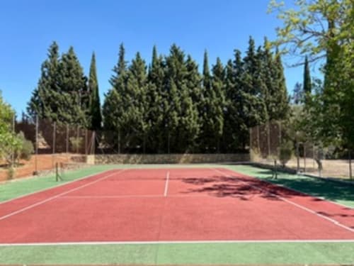 Cancha de tenis rodeada de cipreses en el hotel Holiday Dreams Ronda en Ronda, España, con vistas a las montañas y cielo despejado