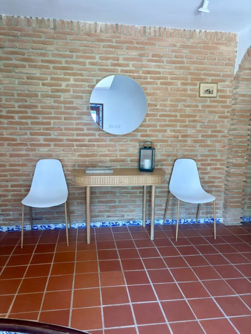 Zona de descanso moderna en Holiday Dreams Ronda con espejo redondo, mesa de madera y sillas blancas contra pared de ladrillo