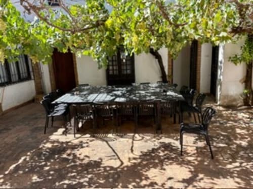Patio sombreado con comedor en Holiday Dreams Ronda, mesas, sillas negras y viñas en el techo