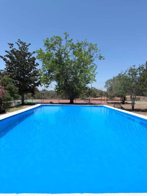 Piscina rectangular azul brillante con ribete blanco en Holiday Dreams Ronda, rodeada de árboles maduros y canchas de tenis