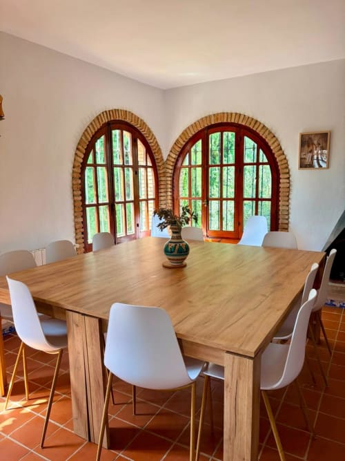 Comedor de Heredad La Encarnación con mesa de madera, sillas blancas y ventanas arqueadas con vistas a las montañas de Ronda