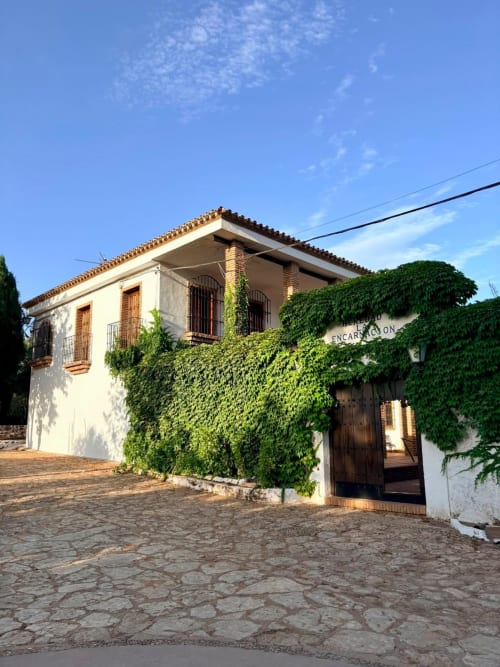 Fachada blanca cubierta de hiedra del Heredad La Encarnación en Holiday Dreams Ronda, España, con tejado de barro y puertas de madera