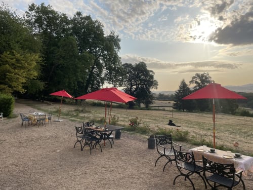 Red umbrellas shade outdoor dining tables at Château de Vaux Morvan in Étang sur Arroux, France, with countryside views.