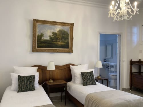 Camas gemelas con sábanas blancas y cojines verdes en la elegante habitación del manor de Mirepoix con cabecera de madera y marcos dorados