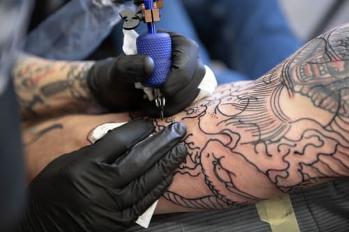 Tatoueur à l'auberge Yasi Hostel Lyon réalisant un motif complexe en encre noire sur le bras d'un client