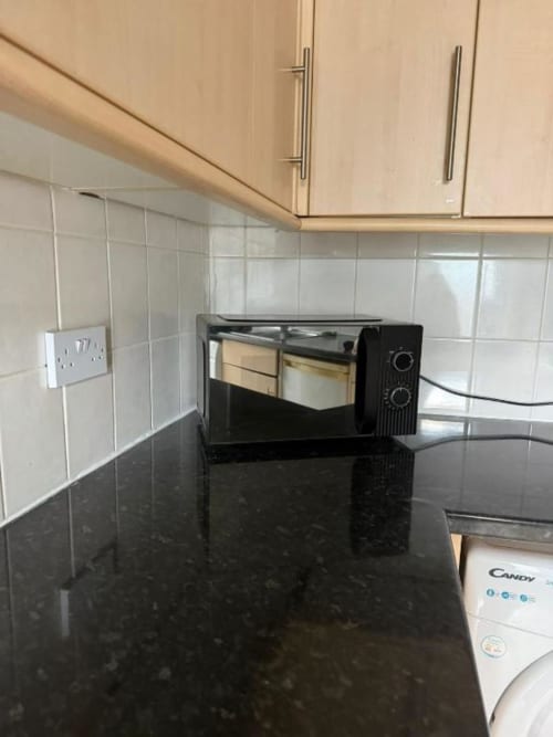 Modern kitchen at Catherines House Kings Cross with black countertop, white tile backsplash, light wood cabinets, and black