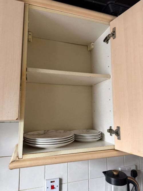 Open wooden kitchen cabinet with white interior shelving storing stacked plates at Catherines House Kings Cross London