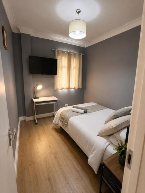 Modern bedroom at Catherines House Kings Cross with grey walls, double bed, TV, desk lamp, and wooden flooring