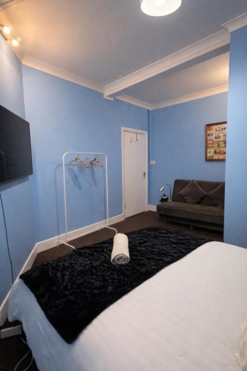 Modern blue bedroom at Catherines House Kings Cross with black bed, dark sofa, TV, and white ceiling beams