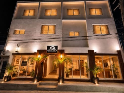 Fachada iluminada nocturna del Hotel Isla Holbox Centro, entrada de planta baja con plantas y habitaciones con luz