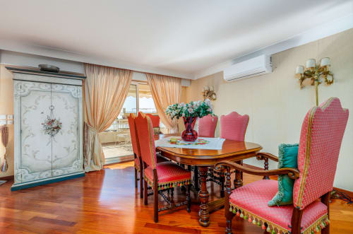 Élégante salle à manger à Riviera Home avec table en bois ouvragé, chaises garnies rose, balcon vue mer et décoration