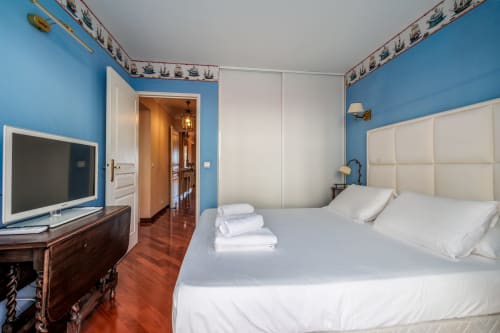 Chambre lumineuse bleu vif à Riviera Home à Roquebrune-Cap Martin avec lit blanc, tête de lit crème et mobilier en bois