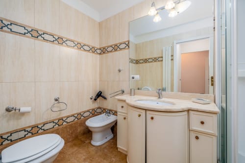 Salle de bain élégante de l'appartement Riviera Home avec carrelage beige, lavabo, toilettes, bidet et bordure décor