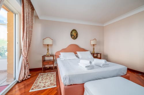 Chambre élégante à Riviera Home avec balcon vue mer, tête de lit en terre cuite, draps blancs, parquet et style période