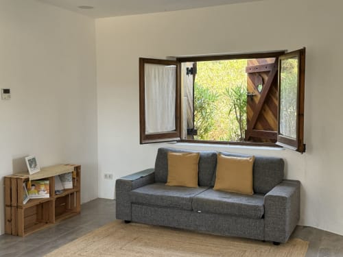 Sofà gris amb coixins grocs davant finestra amb vistes al jardí a l'apartament Séncies Can Girona, Sitges