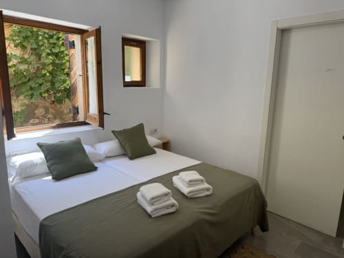 Luminoso dormitorio en Séncies Can Girona de Sitges con ropa de cama en verde, vistas al jardín y patio cubierto de hiedra