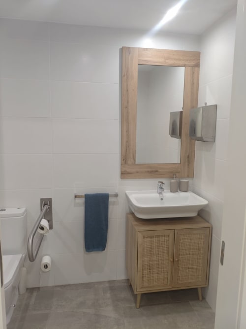 Bany modern de l'apartament Séncies Can Girona a Sitges amb mirall de marc de fusta, lavabo blanc i armari de tocador de rotang