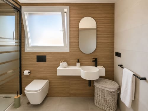 Baño moderno en el apartamento Filliña de Holibai en Baiona con paredes de madera, lavabo flotante, inodoro, espejo redondo y