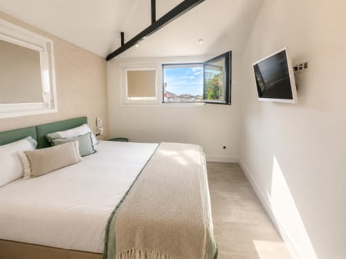Moderno dormitorio en apartamento Holibai Baiona con vistas al mar, cabecero verde, TV mural y grandes ventanales
