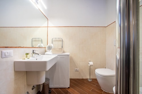 Bagno moderno nell'appartamento di Verona con lavabo bianco, WC, piastrelle beige e pavimento in legno