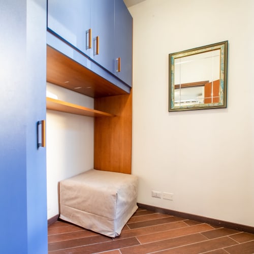 Elegante alcova in camera da letto di appartamento veronese con mobili blu, scaffalature in legno, pouf beige e specchio incorniciato