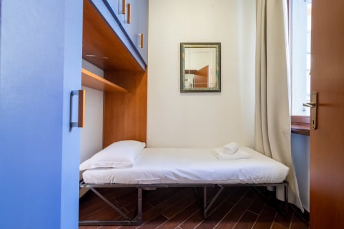 Camera compatta dell'appartamento VIVA SRL a Verona con letto singolo, scaffali in legno, specchio e tende beige