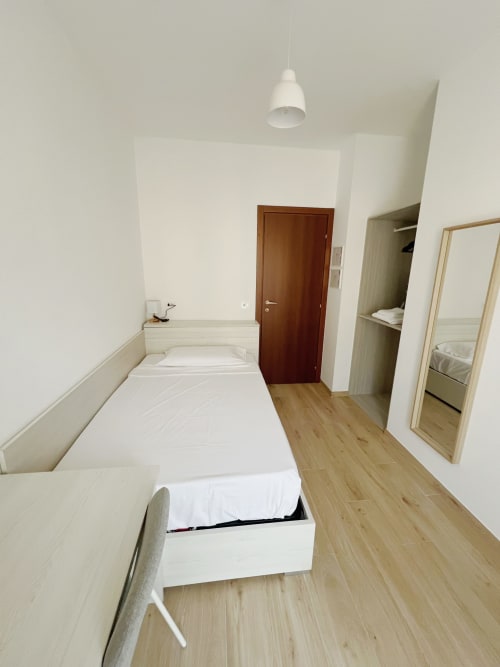 Camera luminosa al Seveso Milan Central Rooms con biancheria bianca, pavimento in legno, specchio, armadio e ingresso marrone
