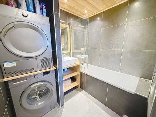 Modern bathroom with stacked washer-dryer, sink, shower enclosure and wooden shelving at Les Tanières de Montgenèvre