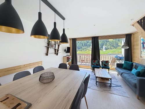 Modern open-plan dining and living room with mountain views, black pendant lights, wooden table, and blue sofa at Les