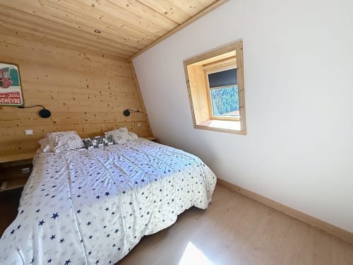 Cozy wooden bedroom in Les Tanières duplex with star-patterned bedding, mountain views through skylight window