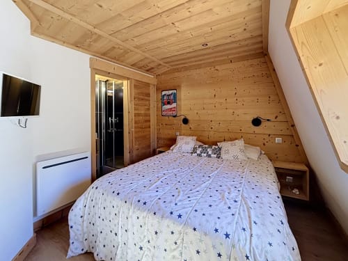 Wood-paneled bedroom with double bed, star-patterned bedding, TV, and modern bathroom at Les Tanières de Montgenèvre