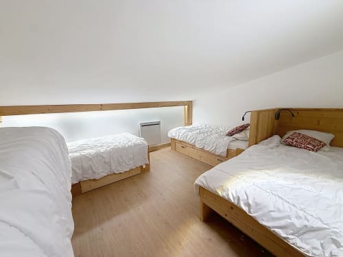 Cozy attic bedroom in Les Tanières duplex with three wooden beds, white linens, and sloped ceiling at Montgenèvre
