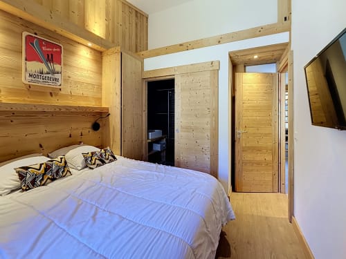 Modern wooden bedroom with double bed, decorative pillows, and doors opening to ensuite bathroom at Les Tanières de
