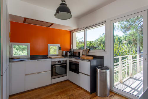 Cuisine contemporaine de la Villa Cloudbreak avec mur d'accent orange, comptoirs noirs, électroménagers en acier inoxydable et vue sur le jardin