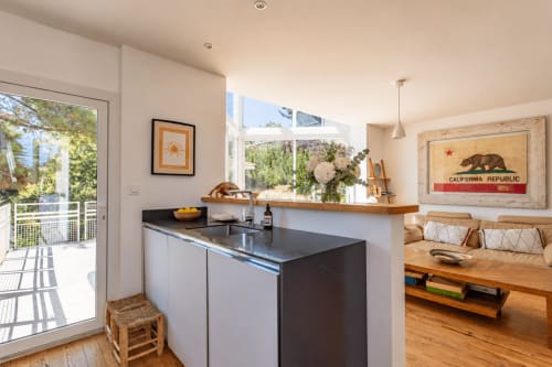 Cuisine ouverte moderne et séjour avec plan de travail noir, parquet, vue sur jardin et décoration Californie