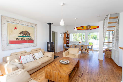 Spacieuse villa, salon avec canapé crème, table basse en bois, art drapeau Californie, décor surf, cheminée et vue mer