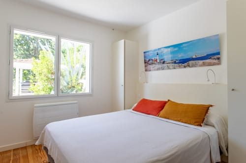 Chambre lumineuse avec lit queen-size, coussins rouges et dorés, décoration côtière, vue sur le jardin à la Villa Cloudbreak, Lège