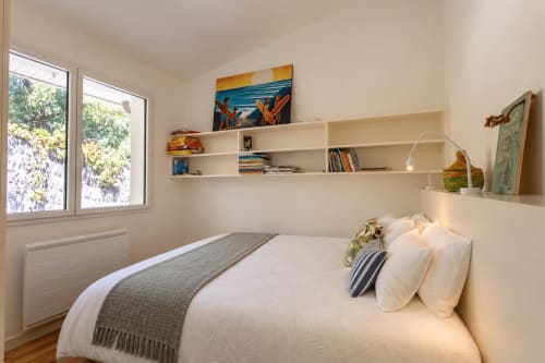 Chambre lumineuse à Villa Cloudbreak avec lit blanc, étagères flottantes, grandes fenêtres sur le jardin et décor côtier