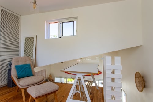 Espace de travail mezzanine moderne avec fauteuil beige, bureau et balustrade en verre, lumière naturelle à Villa Cloudbreak