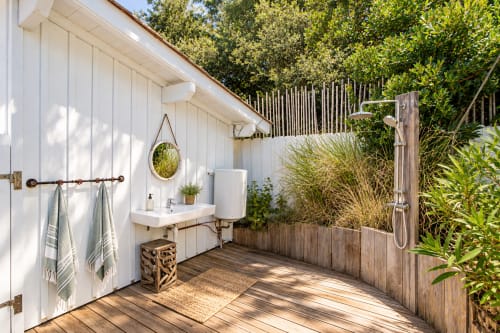Salle de bain extérieure à la Villa Cloudbreak avec lavabo, miroir, douche et terrasse en bois entourée de verdure près de Lège Cap Ferret