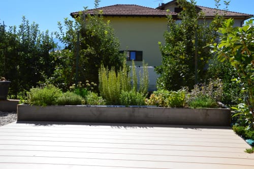 Giardino cortilizio moderno a Villa Rosati a Sanzeno con fioriere rialzate, terrazza in legno contemporaneo e lussureggiante vegetazione mediterranea