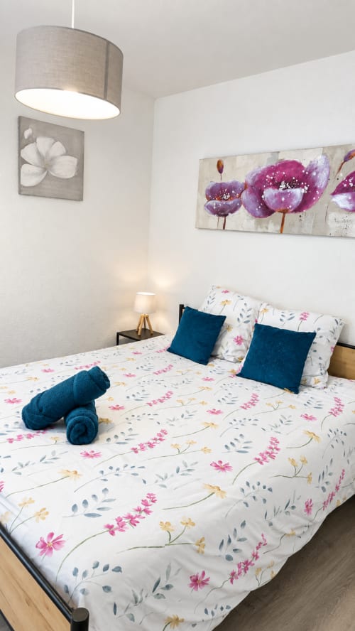 Dormitorio moderno en NN Patrimoine Annemasse con ropa de cama floral, almohadas azules, lámpara colgante y arte floral