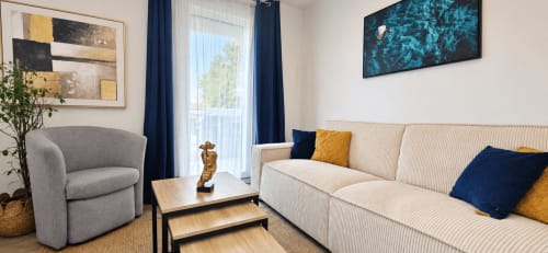 Sala de estar moderna en NN Patrimoine, Annemasse con sofá crema, sillón gris, detalles azules y vistas a las montañas