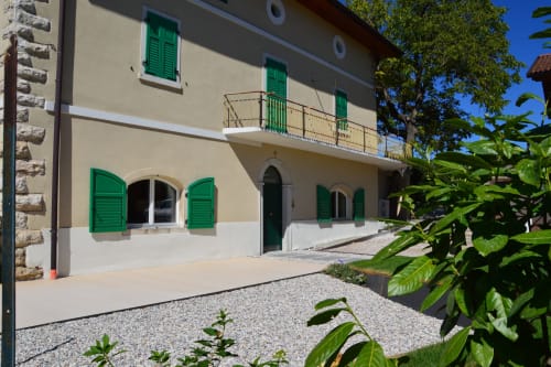 Facciata di Villa Rosati a Sanzeno con persiane verdi, balcone, finestre ad arco e corte in ghiaia
