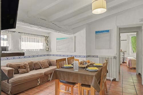 Comedor de Casa El Graner en Girona con sofá marrón, mesa de madera, obras de arte costero y vista al jardín