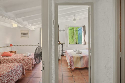 Dos dormitorios contiguos en la casa rural Can Gat Vell en Girona con vigas blancas, suelos de barro y vistas al jardín