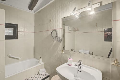 Baño moderno en la casa rural Can Gat Vell con lavamanos, espejo, bañera y paredes alicatadas