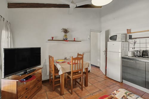 Cocina abierta y comedor con vigas de madera, TV, mesa de comedor, electrodomésticos blancos y suelo de terracota en Can Gat